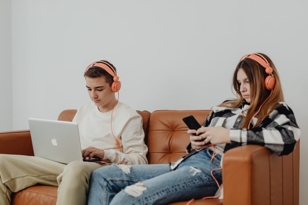 zwei Teenager sitzen auf dem Sofa mit Kopfhörern, Laptop und Smartphone